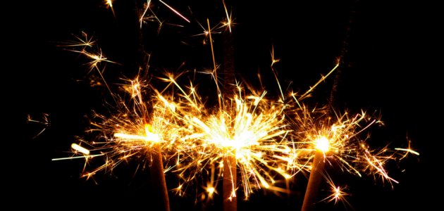 Three sparklers lit up against a dark background, burning down in a moment of celebration.