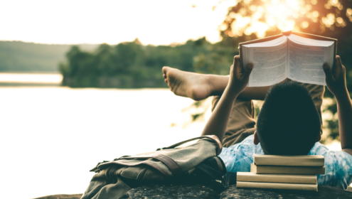 a man sitting by a lake, reading books in the afternoon sun
