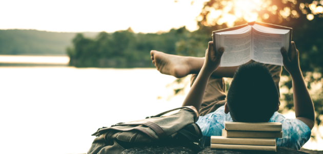 a man sitting by a lake, reading books in the afternoon sun