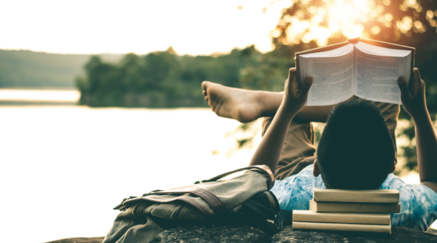 a man sitting by a lake, reading books in the afternoon sun