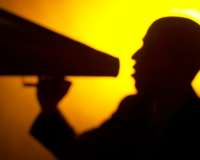a person holding a bullhorn against a yellow backlight. possibly learning to self-direct?