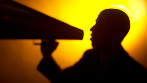 a person holding a bullhorn against a yellow backlight. possibly learning to self-direct?