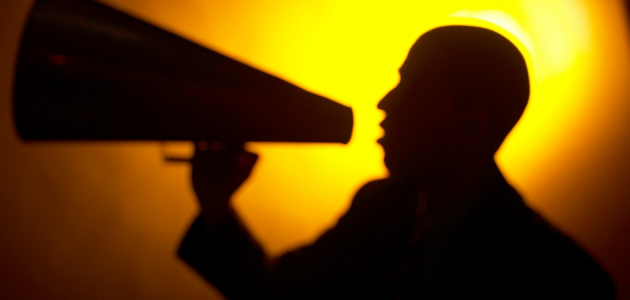 a person holding a bullhorn against a yellow backlight. possibly learning to self-direct?
